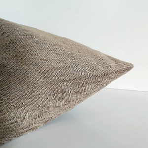 May include: A close-up of a beige pillow with a textured fabric. The pillow is folded in half and the fabric is visible.