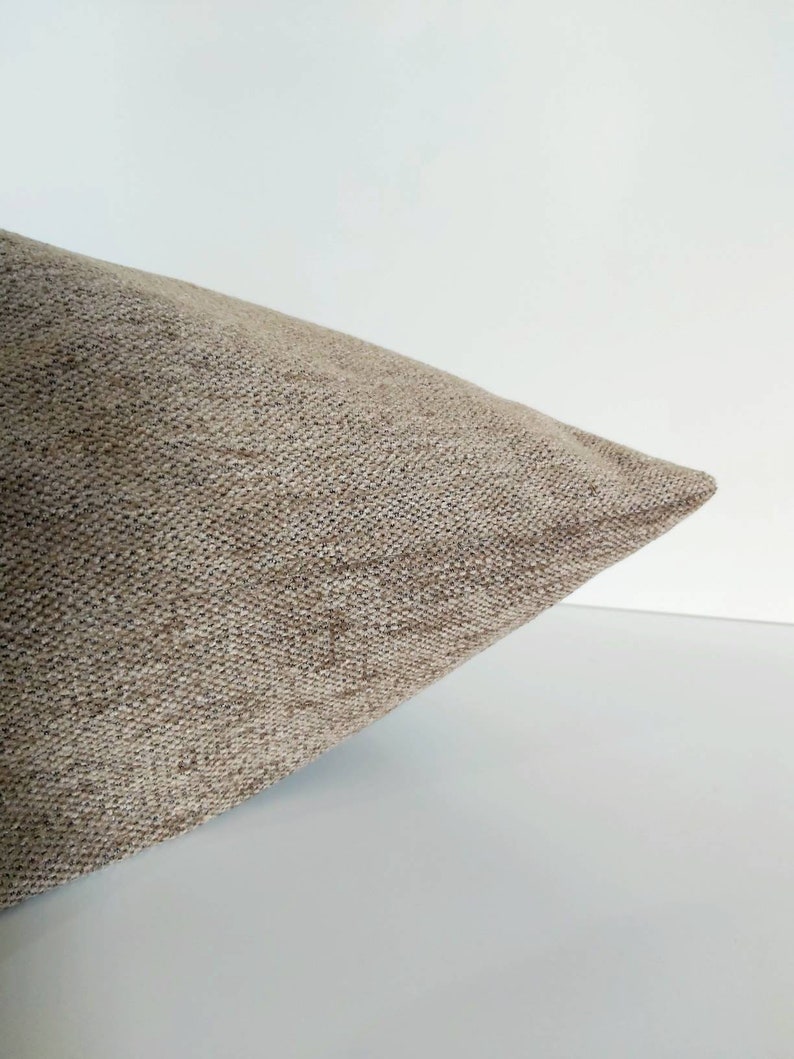 May include: A close-up of a beige pillow with a textured fabric. The pillow is folded in half and the fabric is visible.