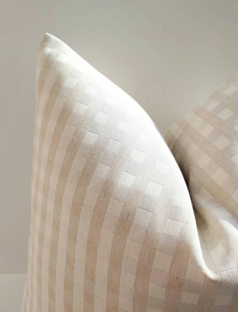 May include: A close-up of a cream-colored pillow with a subtle checkered pattern. The pillow is made of a soft, textured fabric.