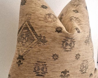 May include: Beige decorative pillow with a woven texture and dark brown geometric patterns. The pillow has a soft, inviting appearance, suitable for adding a touch of style to any living space.
