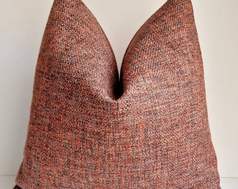 May include: A large, textured throw pillow in shades of rust, orange, and black. The pillow has a woven appearance and a soft, inviting look. The pillow is a square shape and is designed for decorative use on a sofa or bed.