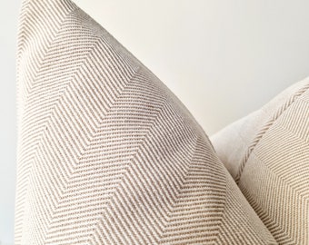 May include: Two beige throw pillows with a subtle herringbone pattern. The pillows are made of a soft, woven fabric.