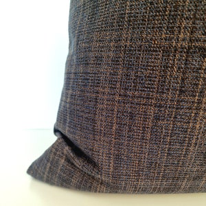 May include: A close-up of a dark blue pillow with a subtle brown woven pattern. The pillow is made of a soft, textured fabric.