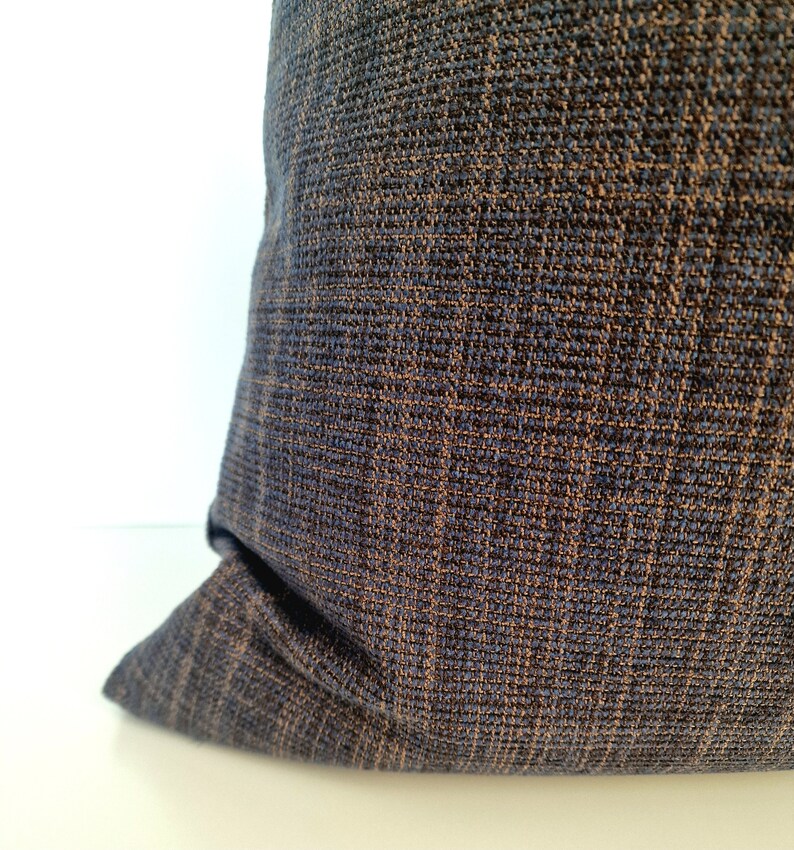 May include: A close-up of a dark blue pillow with a subtle brown woven pattern. The pillow is made of a soft, textured fabric.