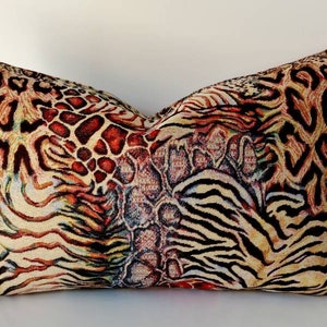 Puede incluir: Una almohada decorativa con un diseño de estampado animal multicolor. El estampado presenta una combinación de patrones de leopardo, cebra y jirafa en tonos marrones, naranjas, amarillos, negros y blancos.