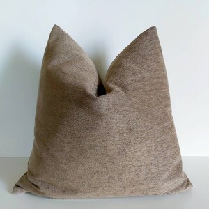 May include: A brown throw pillow with a textured fabric. The pillow is square shaped and has a simple design.