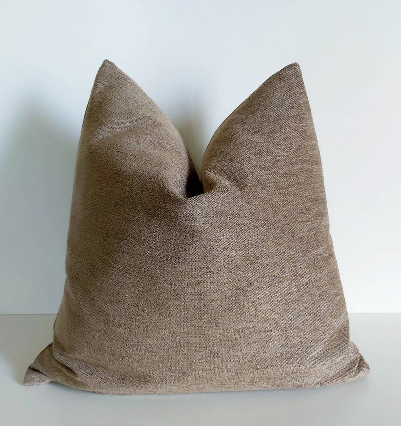 May include: A brown throw pillow with a textured fabric. The pillow is square shaped and has a simple design.
