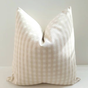 May include: A cream-colored pillow with a subtle checkered pattern. The pillow is made of a soft, woven fabric and has a square shape.