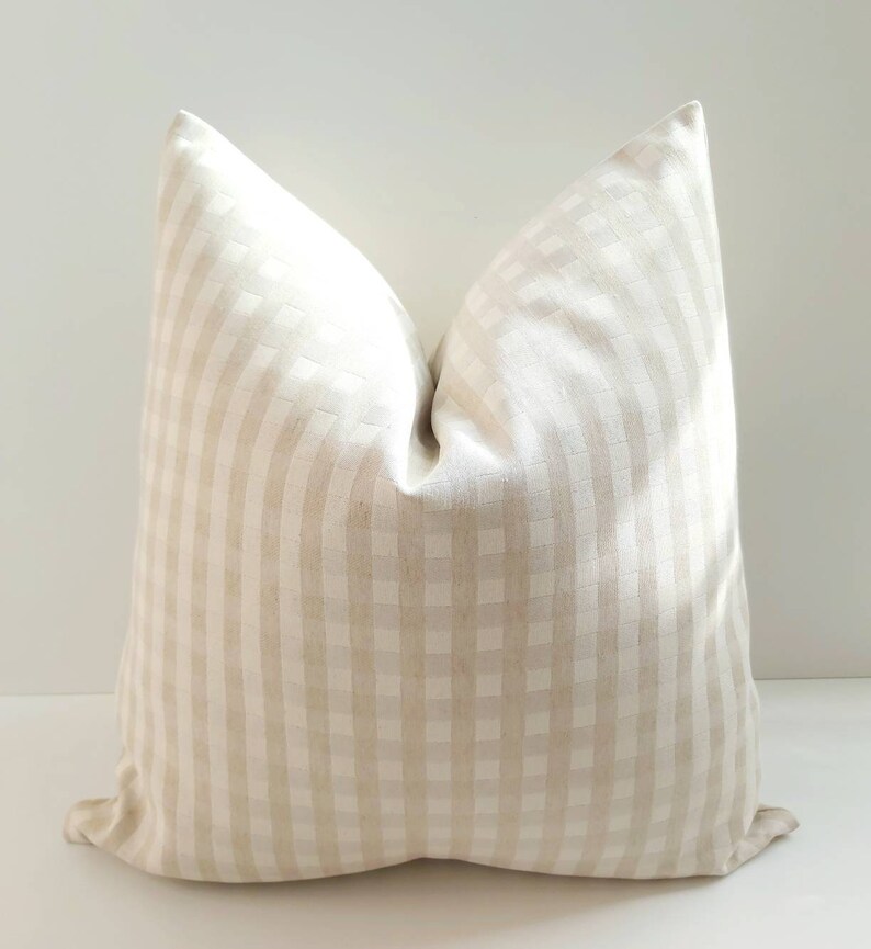 May include: A cream-colored pillow with a subtle checkered pattern. The pillow is made of a soft, woven fabric and has a square shape.