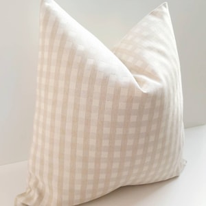 May include: A beige and white gingham pillow with a square pattern. The pillow is made of a soft, textured fabric.