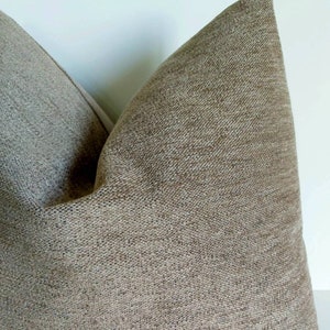 May include: A close-up of a brown pillow with a textured fabric. The pillow is made of a soft, woven material.