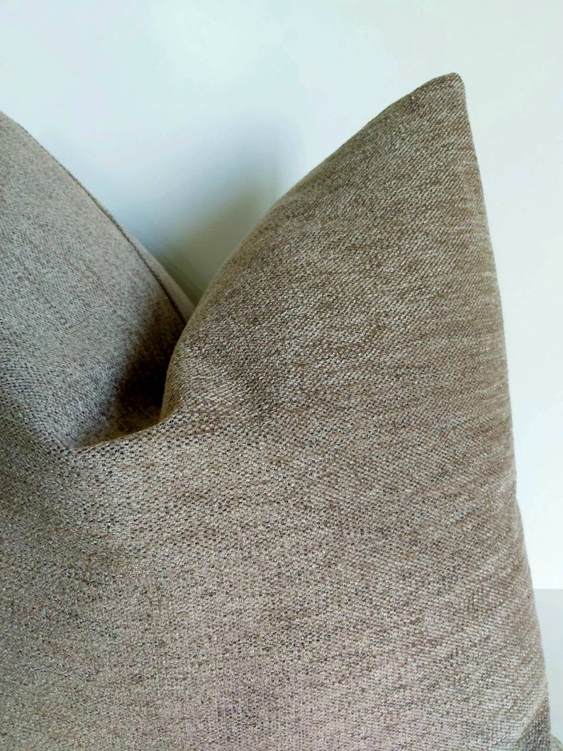 May include: A close-up of a brown pillow with a textured fabric. The pillow is made of a soft, woven material.