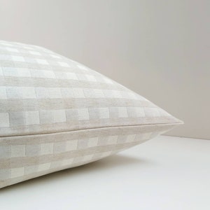 May include: A white and beige gingham pillow with a subtle texture. The pillow is folded in half and the fabric is smooth and soft.
