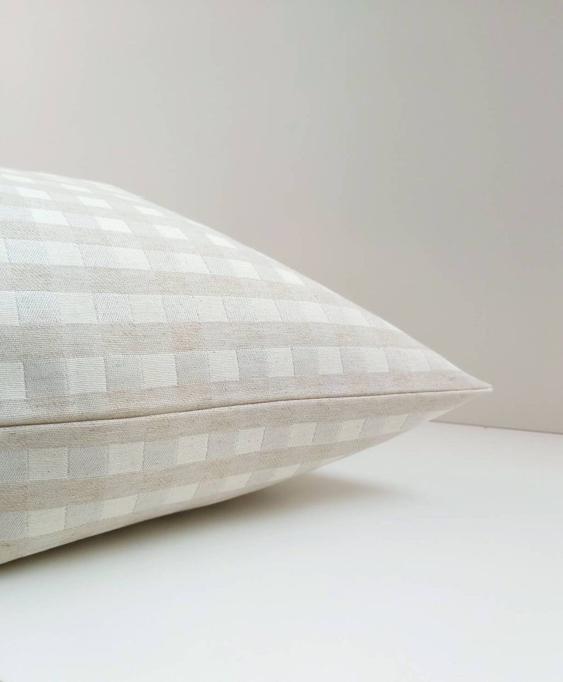 May include: A white and beige gingham pillow with a subtle texture. The pillow is folded in half and the fabric is smooth and soft.