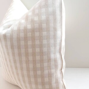 May include: A beige and white gingham pillow with a square pattern. The pillow is made of a soft, woven fabric and has a subtle sheen.