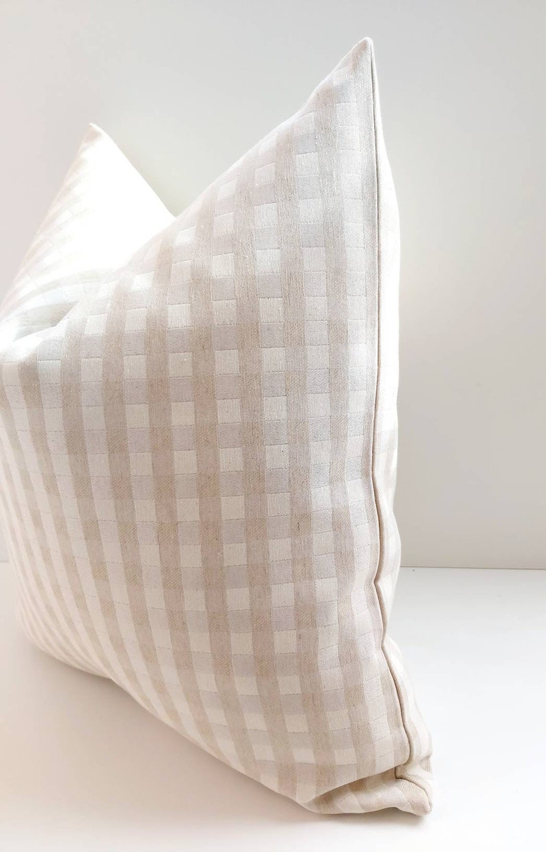 May include: A beige and white gingham pillow with a square pattern. The pillow is made of a soft, woven fabric and has a subtle sheen.