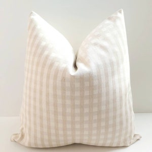 May include: A cream-colored pillow with a subtle gingham pattern. The pillow is made of a soft, textured fabric.