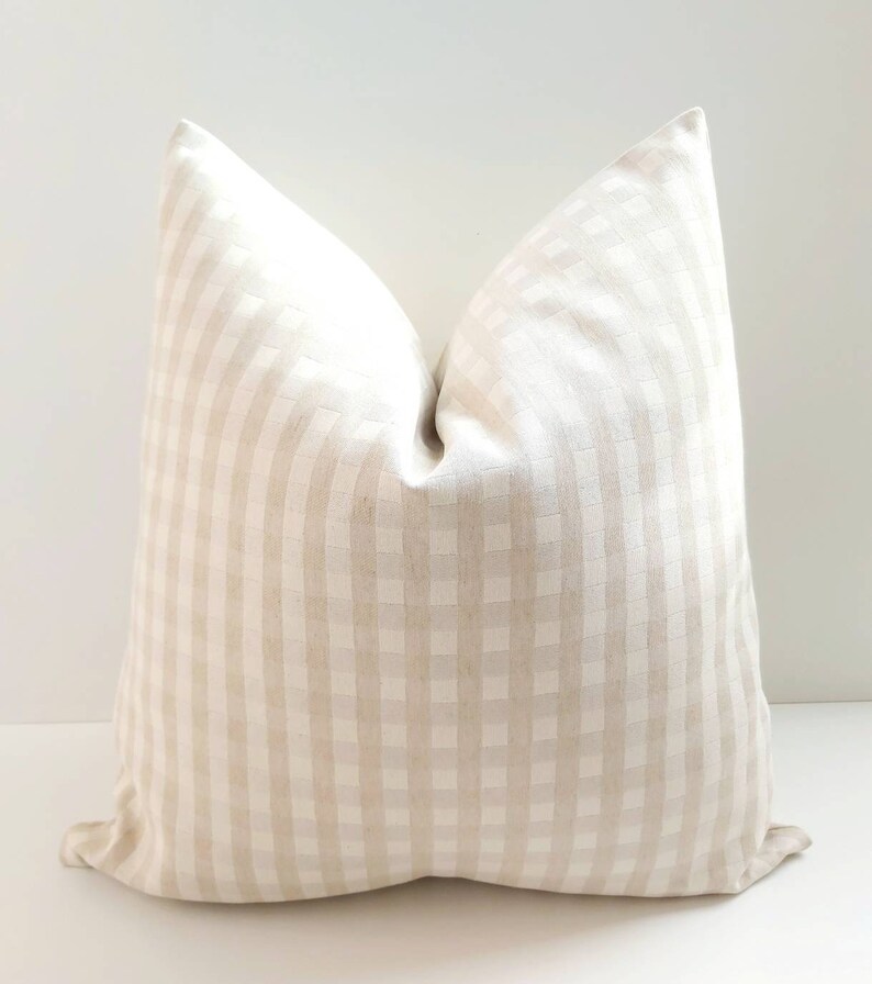May include: A cream-colored pillow with a subtle gingham pattern. The pillow is made of a soft, textured fabric.
