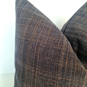 May include: Two dark blue throw pillows with a subtle brown woven pattern. The pillows are made of a soft, textured fabric.