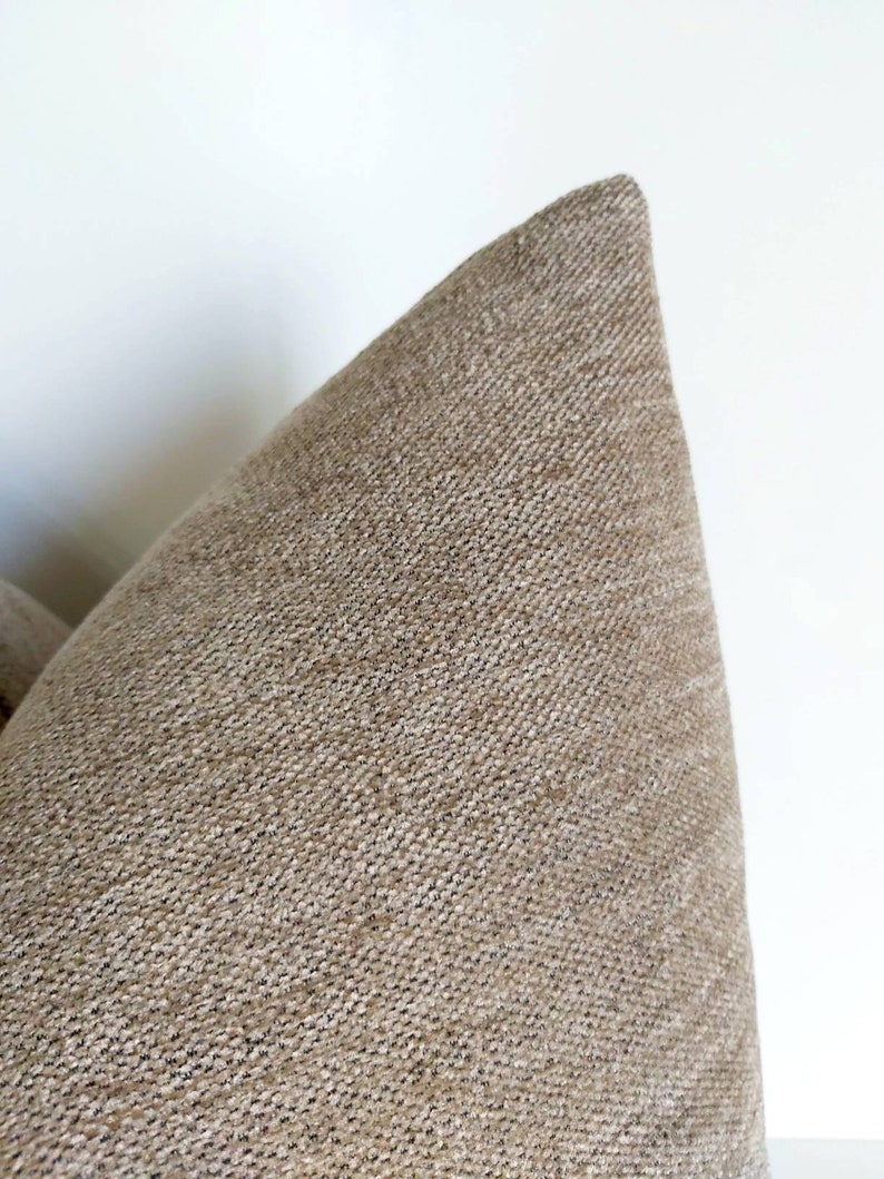 May include: Close-up of a beige throw pillow with a textured fabric. The pillow is made of a soft, woven material.