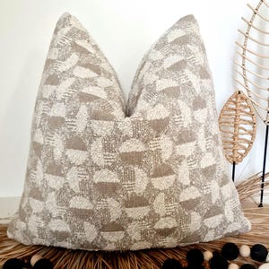 Könnte beinhalten: Ein beige-weißes Dekokissen mit geometrischem Muster. Das Kissen ist aus einem weichen, strukturierten Stoff gefertigt.