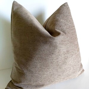 May include: A brown square pillow with a textured fabric. The pillow is made of a soft, woven material.