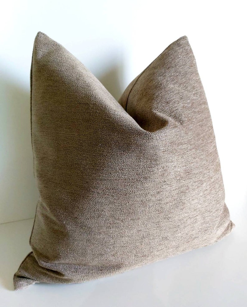 May include: A brown square pillow with a textured fabric. The pillow is made of a soft, woven material.