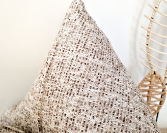 Puede incluir: Primer plano de una almohada beige con tejido tejido texturizado. La almohada tiene forma triangular y un patrón sutil.