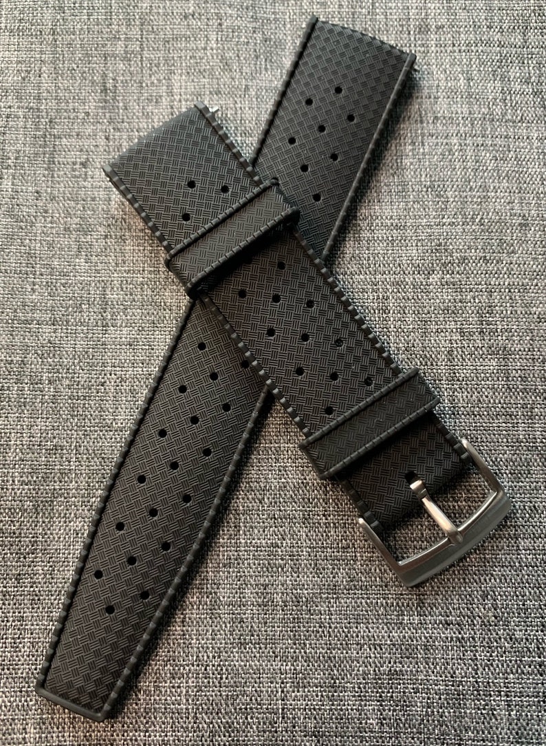 Puede incluir: Dos correas de reloj negras con un patr&oacute;n perforado y una hebilla plateada.