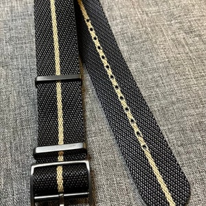 May include: Black watch strap with a white stripe down the center. The strap has a black buckle.