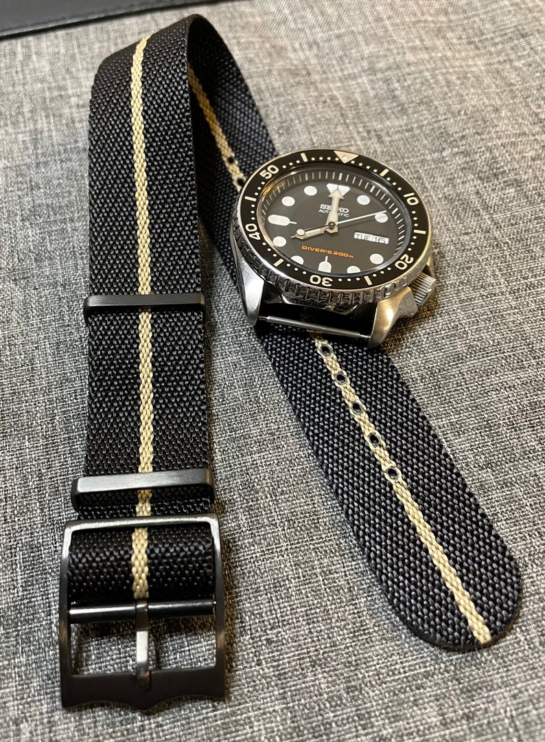 May include: A black and cream striped nylon watch strap with a black buckle. The strap is shown on a silver watch with a black face and black bezel. The watch face has white markings and the text "SEIKO AUTOMATIC DIVERS' 200m".