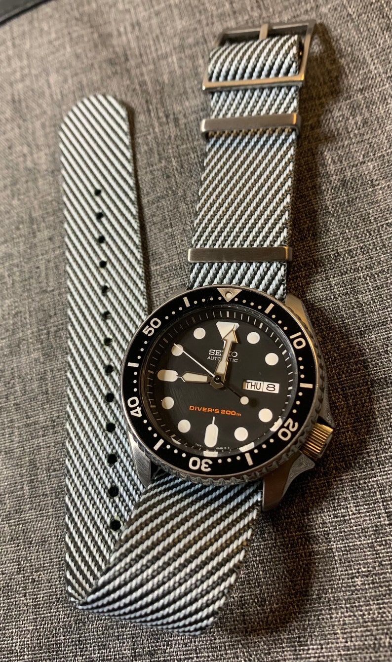 May include: A black and silver Seiko automatic watch with a black face and white markings. The watch has a black and white striped nylon watch band. The watch face says "Diver's 200m" and "Thu 8".