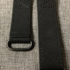 May include: Two black canvas watch straps with metal loops. The straps are stitched with white thread.