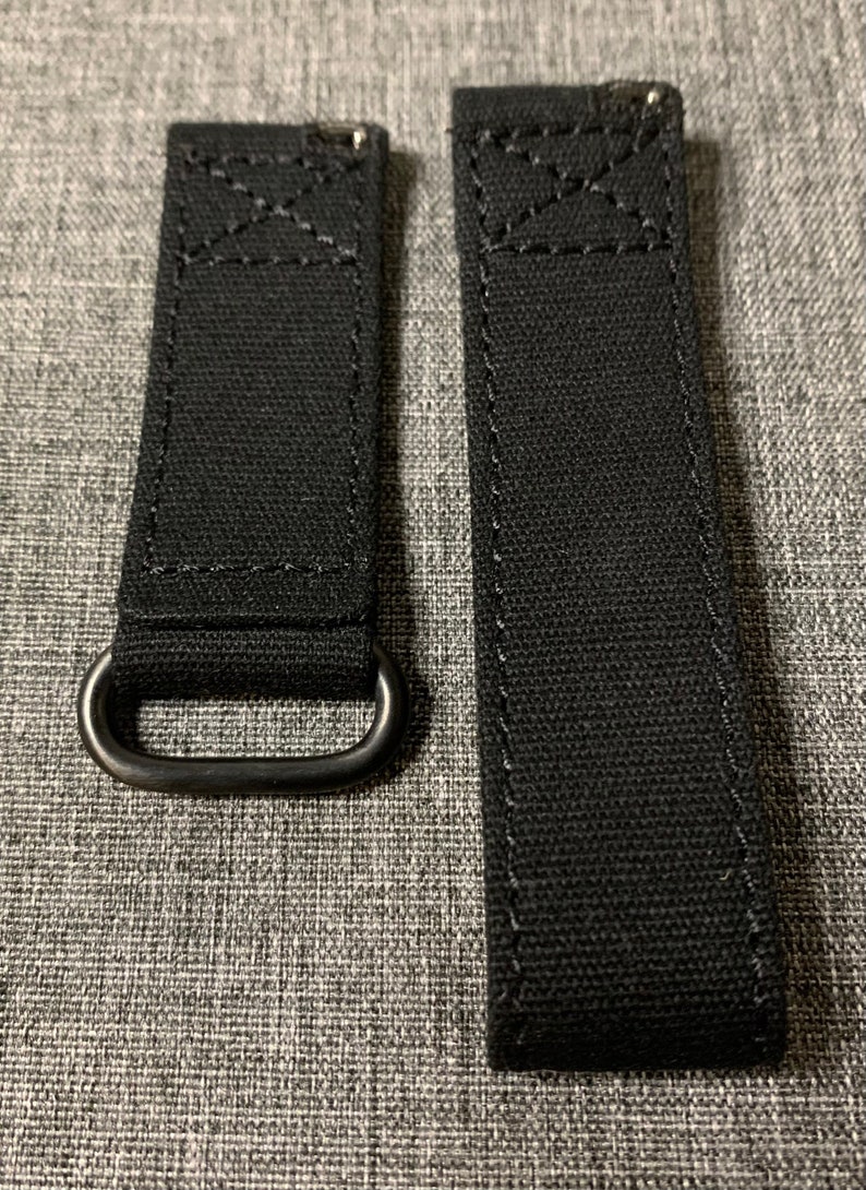 May include: Two black canvas watch straps with metal loops. The straps are stitched with white thread.