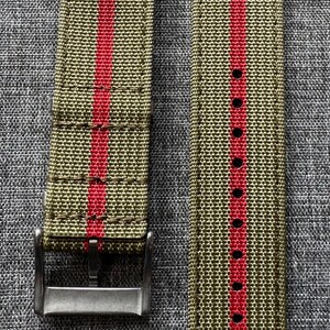 May include: A pair of watch straps with a green and red striped pattern. The straps are made of a woven fabric and have a metal buckle.
