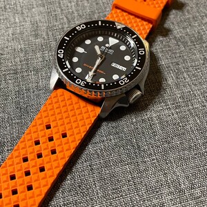 Puede incluir: Un reloj de buceo autom&aacute;tico Seiko negro y plateado con una esfera negra y una correa de caucho naranja. La esfera del reloj tiene marcas blancas y una ventana de fecha que dice "FRI 21".