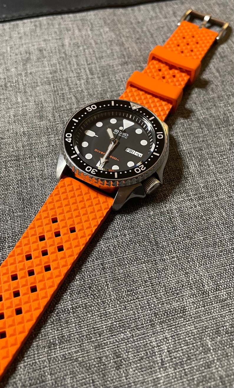 Puede incluir: Un reloj de buceo autom&aacute;tico Seiko negro y plateado con una esfera negra y una correa de caucho naranja. La esfera del reloj tiene marcas blancas y una ventana de fecha que dice "FRI 21".