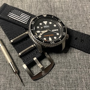 May include: A black Seiko watch with a black and white patterned strap and a silver buckle. The watch face is black with white markings and the text "SEIKO AUTOMATIC" and "DIVER'S 200m".