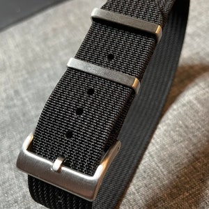 May include: A black nylon watch strap with silver buckle and keeper loops.