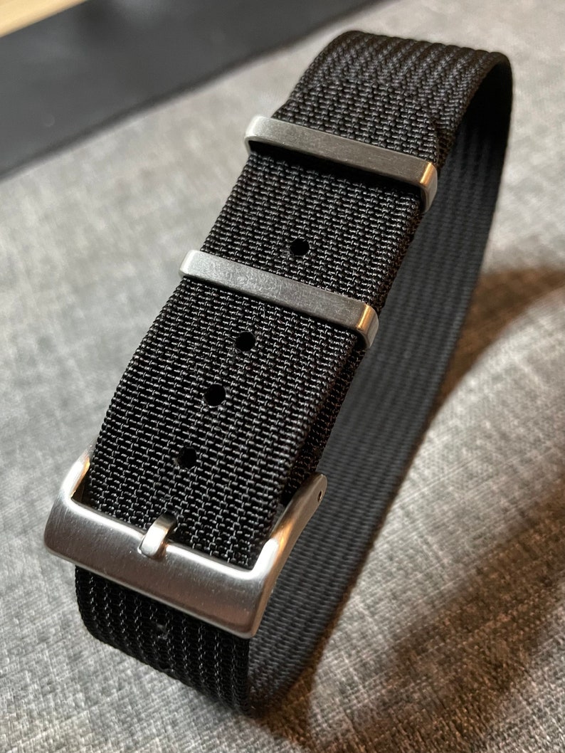 May include: A black nylon watch strap with silver buckle and keeper loops.