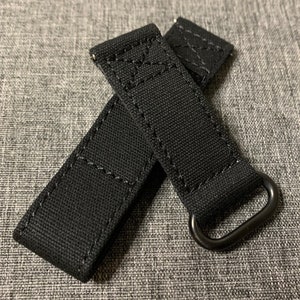 May include: Two black canvas watch straps with black metal buckles. The straps have a stitched design.