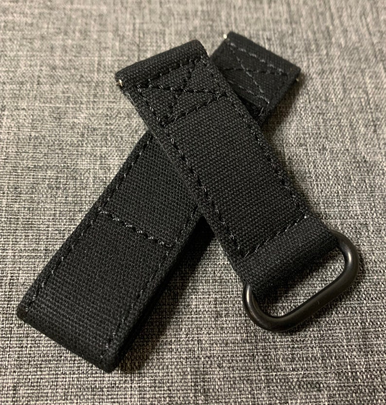 May include: Two black canvas watch straps with black metal buckles. The straps have a stitched design.