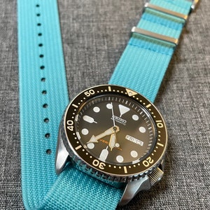 May include: A black and silver wristwatch with a blue nylon watch strap. The watch face has white markings and a date window that reads "FRI 13".