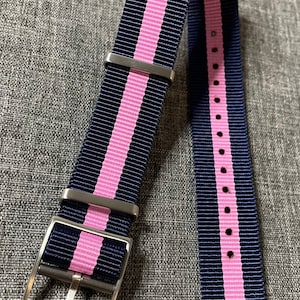 Peut inclure: Un bracelet de montre rayé bleu marine et rose avec une boucle argentée.