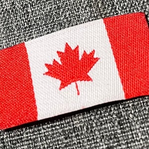 May include: A red and white Canadian flag patch with a red maple leaf in the centre.