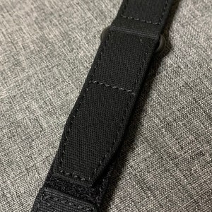 May include: Black watch strap with a metal buckle. The strap is made of a woven fabric.