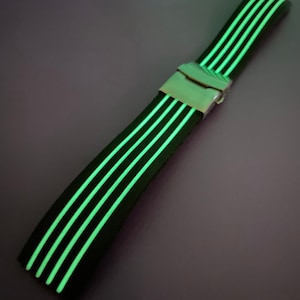 May include: A black watch strap with five glowing green stripes and a silver buckle.