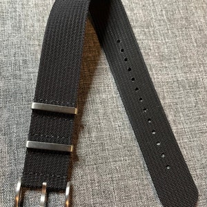 May include: A black nylon watch strap with a silver buckle and three keeper loops.