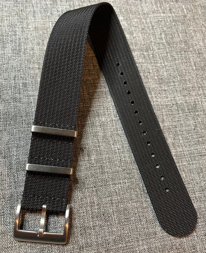 May include: A black nylon watch strap with a silver buckle and three keeper loops.