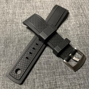 May include: Black rubber watch strap with a textured pattern and a silver buckle.